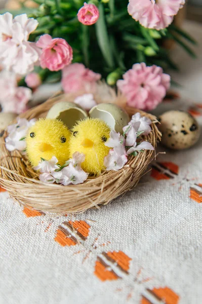 Yumurta kabuklu küçük bir yuvada iki sevimli oyuncak yavrunun yer aldığı neşeli Paskalya 'da hayat devam ediyor. Sahne benekli bıldırcın yumurtaları ve beyaz işlemeli masa örtüsü üzerinde taze pembe karanfil çiçekleriyle çevrilidir. Sıcak, aydınlık ve sıcak bir tatil.