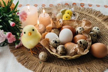 Yüksek açılı, kahverengi ve beyaz tavuk yumurtalarının yeniden kullanılabilir ağ iplik torbasına konulmuş karton bir kutuya konulmuş hali. Sahne, içinde iki tüylü sarı oyuncak civciv ve narin bahar çiçeklerinin bulunduğu küçük bir kuş yuvası ile süslenmiştir.,