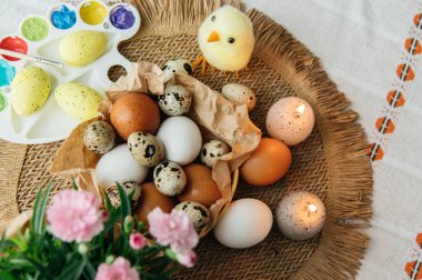 Yüksek açılı, kahverengi ve beyaz tavuk yumurtalarının yeniden kullanılabilir ağ iplik torbasına konulmuş karton bir kutuya konulmuş hali. Sahne, içinde iki tüylü sarı oyuncak civciv ve narin bahar çiçeklerinin bulunduğu küçük bir kuş yuvası ile süslenmiştir.,