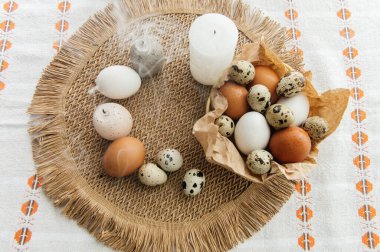 Yüksek açılı, kahverengi ve beyaz tavuk yumurtalarının yeniden kullanılabilir ağ iplik torbasına konulmuş karton bir kutuya konulmuş hali. Sahne, içinde iki tüylü sarı oyuncak civciv ve narin bahar çiçeklerinin bulunduğu küçük bir kuş yuvası ile süslenmiştir.,