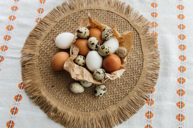 Yüksek açılı, kahverengi ve beyaz tavuk yumurtalarının yeniden kullanılabilir ağ iplik torbasına konulmuş karton bir kutuya konulmuş hali. Sahne, içinde iki tüylü sarı oyuncak civciv ve narin bahar çiçeklerinin bulunduğu küçük bir kuş yuvası ile süslenmiştir.,