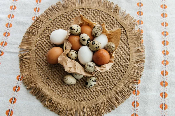 Yüksek açılı, kahverengi ve beyaz tavuk yumurtalarının yeniden kullanılabilir ağ iplik torbasına konulmuş karton bir kutuya konulmuş hali. Sahne, içinde iki tüylü sarı oyuncak civciv ve narin bahar çiçeklerinin bulunduğu küçük bir kuş yuvası ile süslenmiştir.,