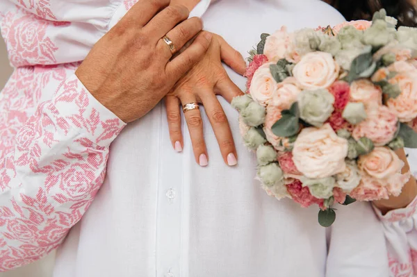 Bir gelin ve damadın, Ukrayna 'dan nakışlı gömlekler giyip, ellerinde güzel bir buket çiçekle alyanslarını gösteren romantik bir yakın plan fotoğrafı..