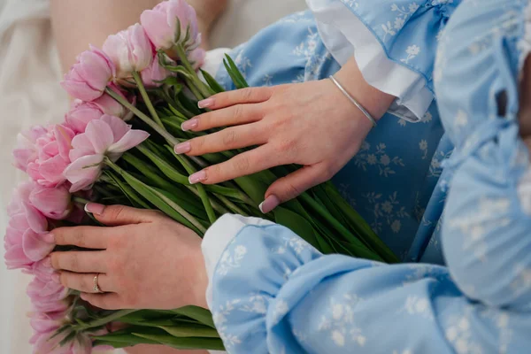 Gökyüzü mavisi bir elbise içinde beyaz detaylar taşıyan genç bir kadın, buruşuk beyaz çarşafların üzerinde dinlenirken yüksek bir açıdan görülüyor. Elinde muhteşem, bol pembe, çok yapraklı çift yapraklı lalelerden oluşan bir buket tutuyor. Çıplak bacakları solda görünüyor..