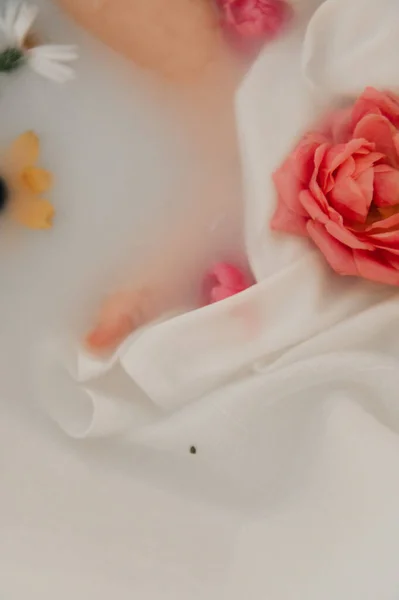 Bir bebeğin küçük ayağının, pembe bir gülle kısmen süt banyosuna batırıldığı yakın plan..