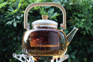 Çayın döküldüğü cam çaydanlık ahşap bir arka planda duruyor.