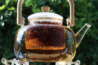 Çayın döküldüğü cam çaydanlık ahşap bir arka planda duruyor.