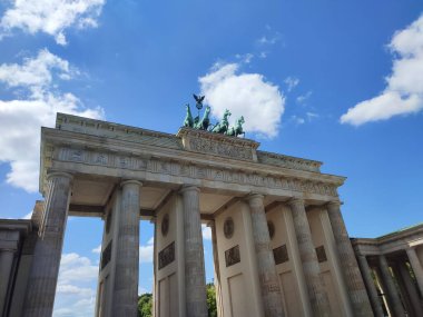 Berlin 'deki Brandenburg Kapısı' nın alçak açılı görüntüsü klasik sütunlar, Quadriga heykelleri ve parlak mavi gökyüzü. Tarihi, kültürü, seyahat ve mimariyi sembolize eden ikonik Avrupa simgesi.