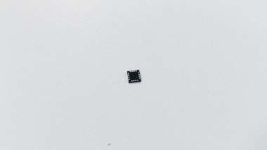 Beyaz yüzeyde metalik temaslı siyah entegre devre çipine yakın plan, akıllı telefon elektroniğinde kullanılır.