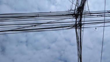 Tayland 'da bulutlu bir gökyüzüne karşı karmaşık teçhizat kabloları, kentsel altyapı zorluklarını ve yoğun elektrik kablosu düzenini vurguluyor.