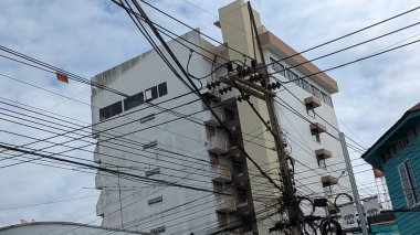 Tayland 'da bulutlu bir gökyüzüne karşı karmaşık teçhizat kabloları, kentsel altyapı zorluklarını ve yoğun elektrik kablosu düzenini vurguluyor.
