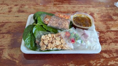 Geleneksel Tayland atıştırmalığı Miang Kham, cha plu yaprakları, kurutulmuş karides, fıstık, acı biber ve plastik paketlerde tatlı-baharatlı sos ile servis edilir..