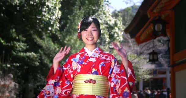 Красивая японская девушка в Кимоно машет перед камерой перед храмом — стоковое видео