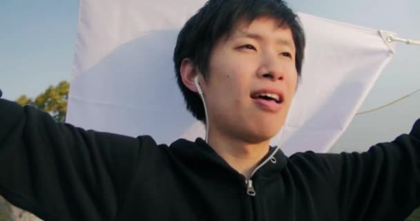 Inspirational young Japanese man holds his nations flag while running looking over city at sunrise 4K — Stock Video