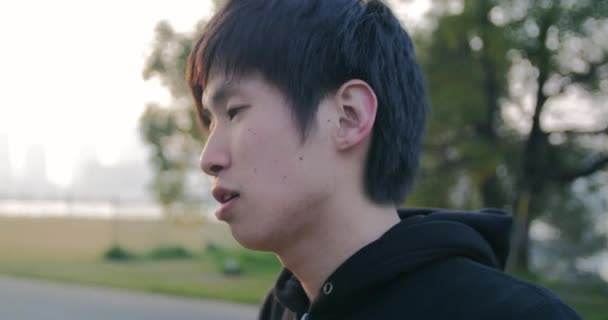 Inspirando joven corredor japonés pone en los auriculares y se prepara para ejecutar 4K — Vídeo de stock