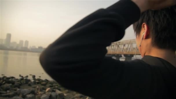 Молодой японский бегун продолжает тепло прыгать вверх и вниз по берегам рек на восходе солнца — стоковое видео