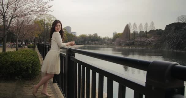 Menina japonesa atraente vestindo vestido branco sorri para a câmera no parque em Osaka, Japão 4K — Vídeo de Stock