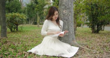 Güzel Japon genç kadınların okuma geniş sürgülü gülümser ve bir ağaç altında 4 k vurdu