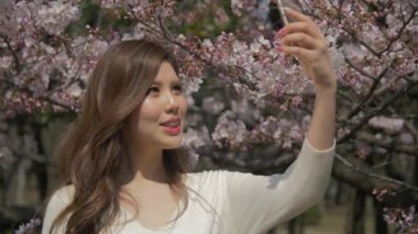 Güzel Japanse kız inanılmaz sakura kiraz çiçeği ağacının yavaş--dan içinde bir selfie alır 