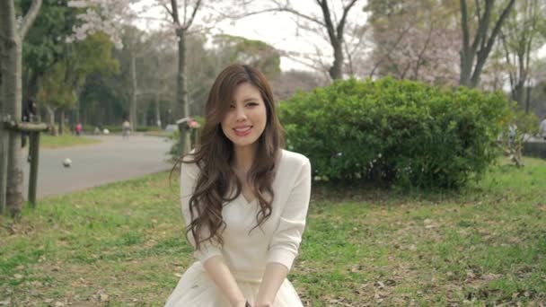 Belle fille japonaise assise sur l'herbe jetant des feuilles dans l'air Mouvement lent — Video