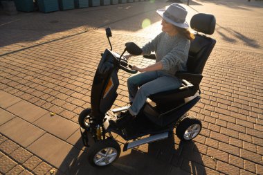 Woman tourist riding a four wheel mobility electric scooter on a city street. clipart
