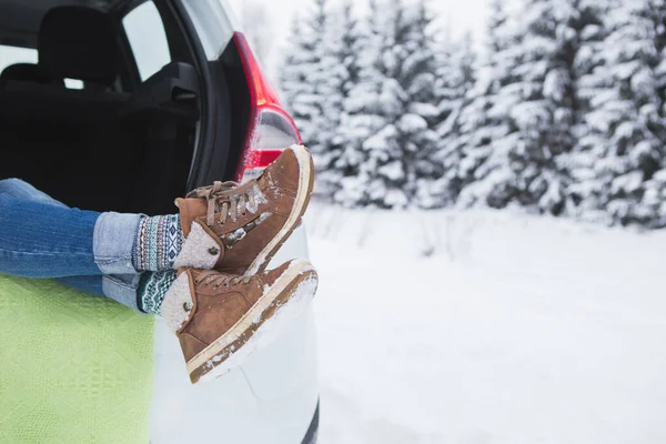 Woman sits in the trunk of the car. Close-up of winter boots
