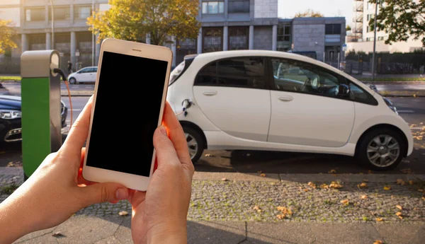 Ręce ze smartfonem na tle wypożyczonego samochodu na stacji ładowania — Zdjęcie stockowe