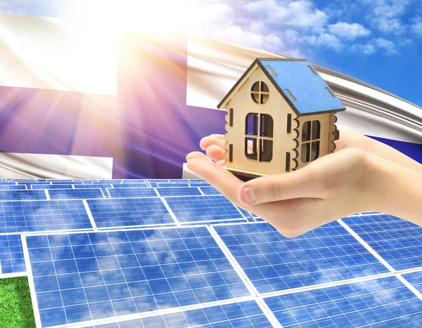 The photo with solar panels and a woman's palm holding a toy house shows the flag of Finland in the sun.