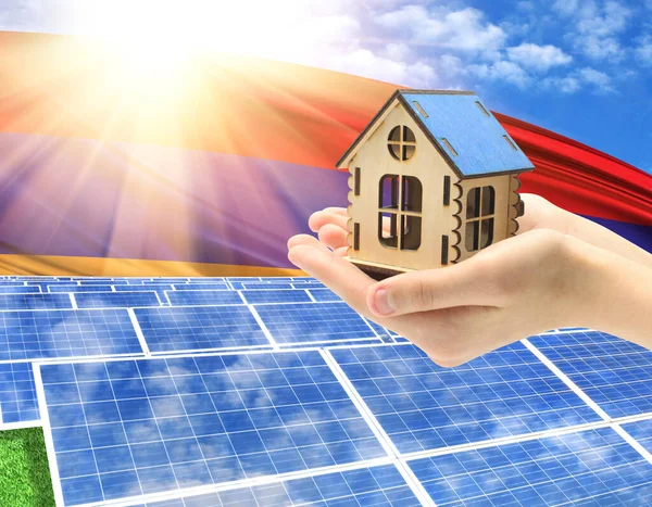 The photo with solar panels and a woman\'s palm holding a toy house shows the flag of Armenia in the sun.