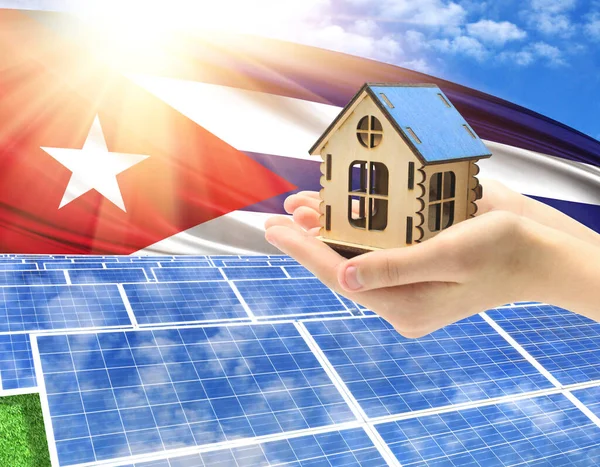 The photo with solar panels and a woman\'s palm holding a toy house shows the flag of Cuba in the sun.