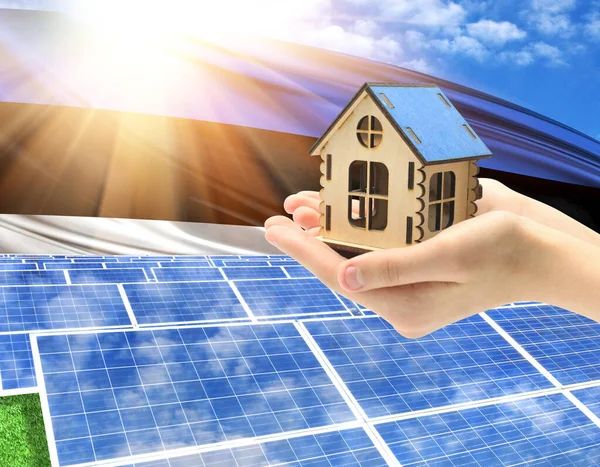 The photo with solar panels and a woman\'s palm holding a toy house shows the flag of Estonia in the sun.