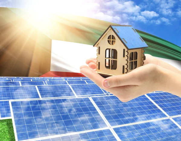 The photo with solar panels and a woman\'s palm holding a toy house shows the flag of Kuwait in the sun.