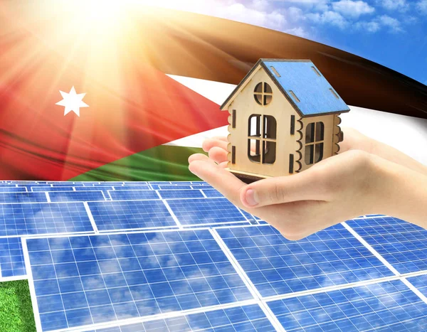 The photo with solar panels and a woman\'s palm holding a toy house shows the flag of Jordan in the sun.