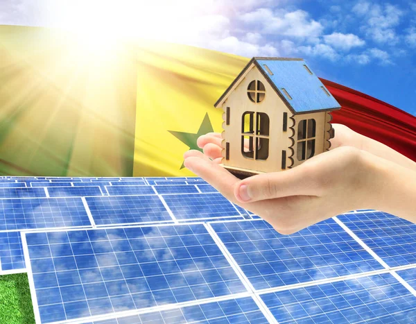 The photo with solar panels and a woman\'s palm holding a toy house shows the flag of Senegal in the sun.