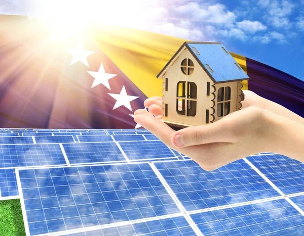The photo with solar panels and a woman\'s palm holding a toy house shows the flag of Bosnia and Herzegovina in the sun.