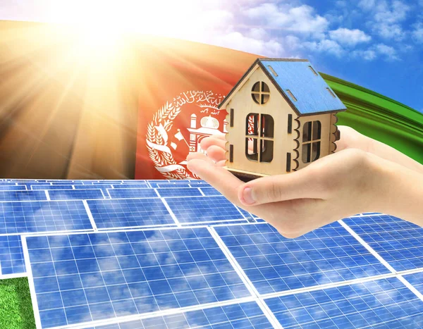 The photo with solar panels and a woman\'s palm holding a toy house shows the flag of Afghanistan in the sun.