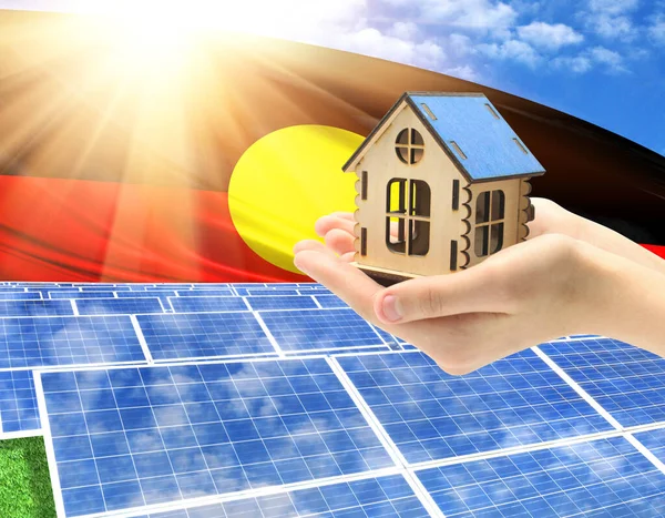 The photo with solar panels and a woman\'s palm holding a toy house shows the flag of Australian Aboriginal in the sun.