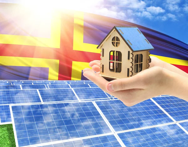 The photo with solar panels and a woman\'s palm holding a toy house shows the flag of Aland in the sun.