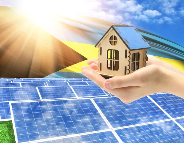 The photo with solar panels and a woman\'s palm holding a toy house shows the flag of Bahamas in the sun.
