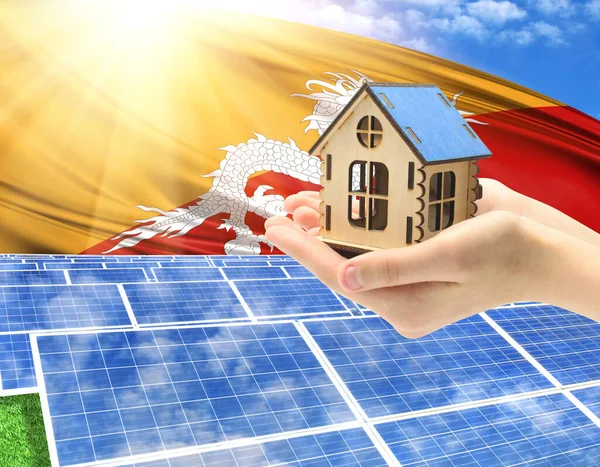 The photo with solar panels and a woman\'s palm holding a toy house shows the flag of Butane in the sun.