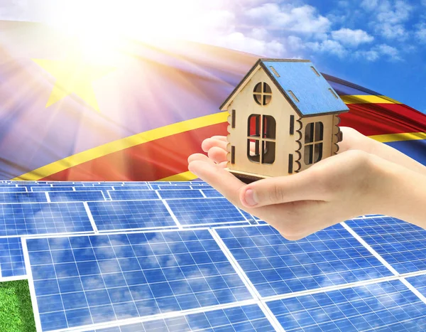 The photo with solar panels and a woman's palm holding a toy house shows the flag of Congo Democratic in the sun.