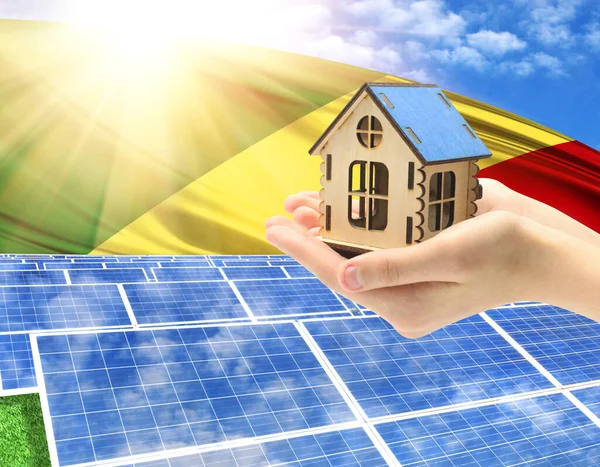 The photo with solar panels and a woman's palm holding a toy house shows the flag of Congo,Republic in the sun.