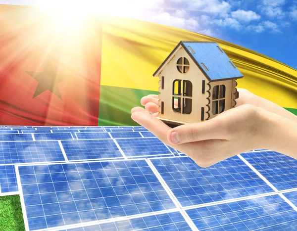 The photo with solar panels and a woman\'s palm holding a toy house shows the flag of Guinea Bissau in the sun.