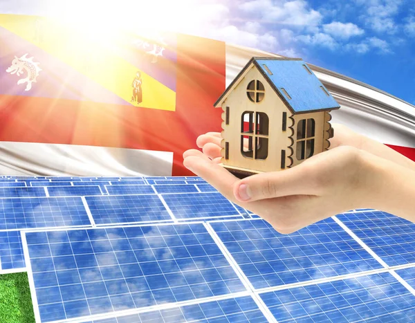 The photo with solar panels and a woman\'s palm holding a toy house shows the flag of Herm in the sun.