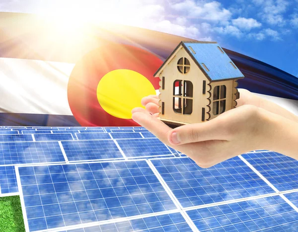 The photo with solar panels and a woman\'s palm holding a toy house shows the flag State of Colorado in the sun.
