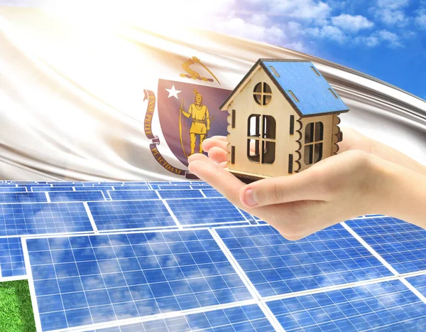 The photo with solar panels and a woman\'s palm holding a toy house shows the flag State of Massachusetts in the sun.