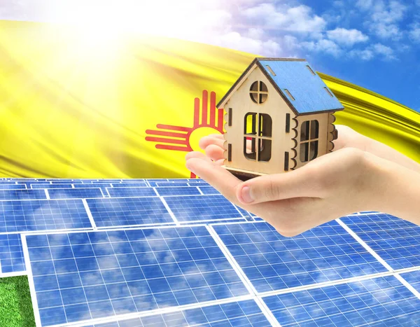 The photo with solar panels and a woman\'s palm holding a toy house shows the flag State of New Mexico in the sun.