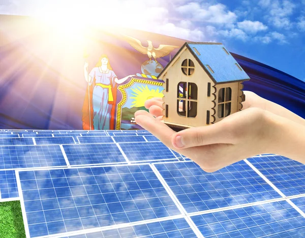 The photo with solar panels and a woman\'s palm holding a toy house shows the flag State of New York in the sun.