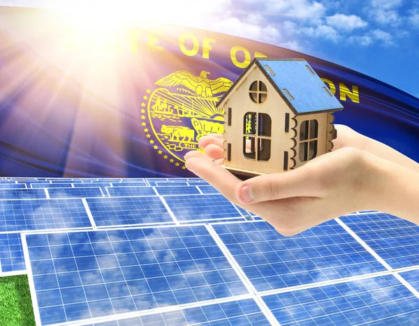 The photo with solar panels and a woman\'s palm holding a toy house shows the flag State of Oregon in the sun.