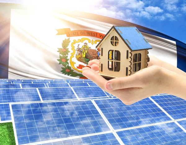 The photo with solar panels and a woman\'s palm holding a toy house shows the flag State of West Virginia in the sun.